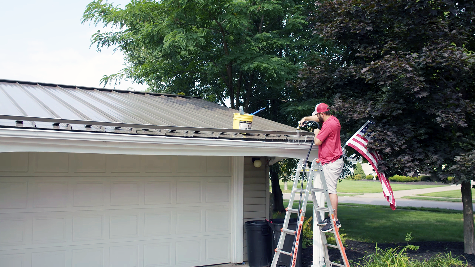 A professional roofing contractor standing on a ladder in the process of repainting a metal roof 