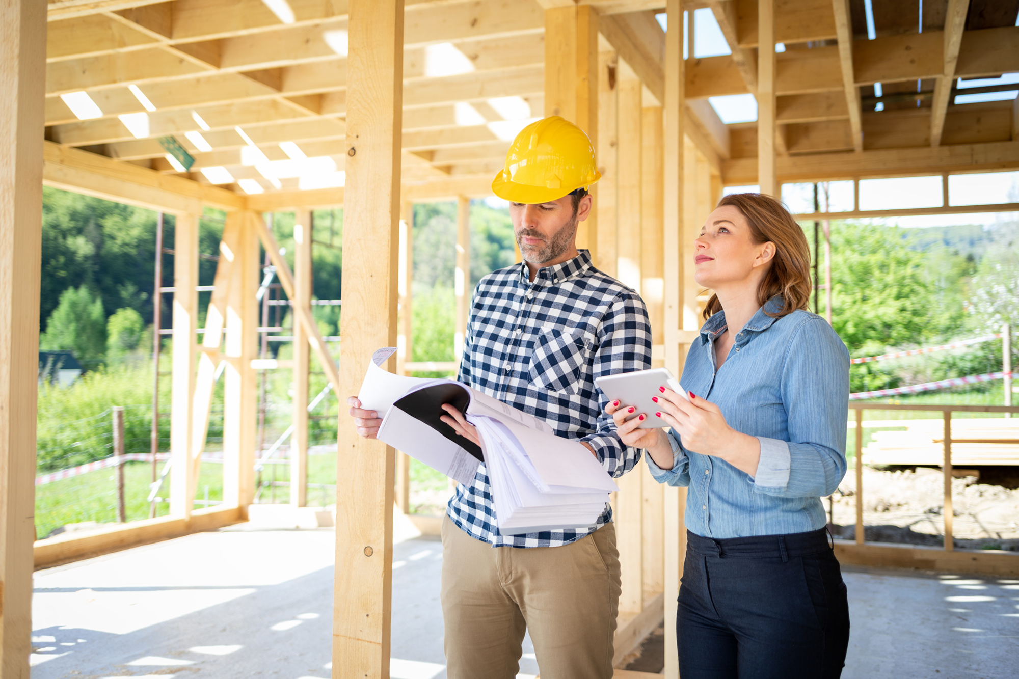 A man in a hardhat looks over home building plans alongside a woman holding a tablet 