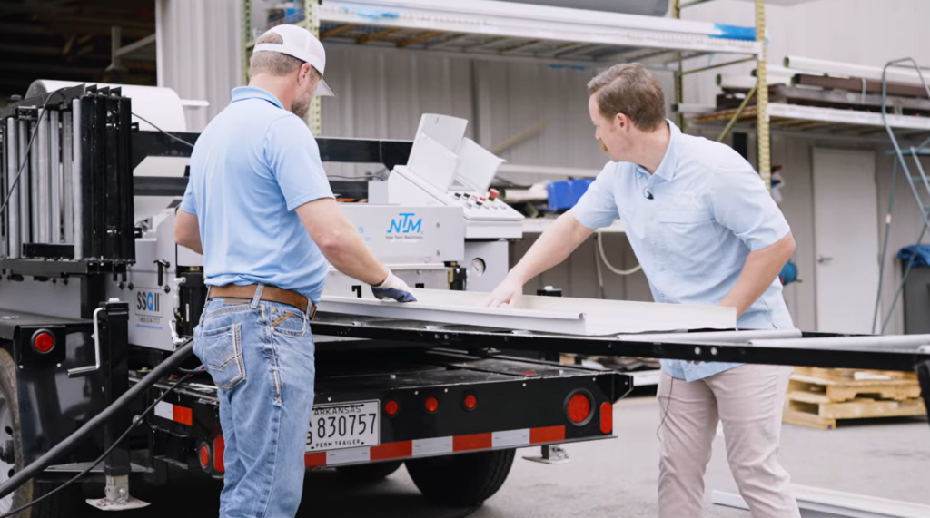 Two men running Sheffield Metals materials out of an NTM portable rollforming mahcine